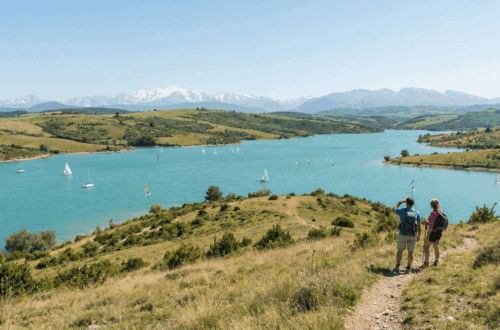 Vue panoramique sur le Lac de la Ganguise aux eaux turquoise avec activités nautiques et la chaîne des Pyrénées en arrière-plan.